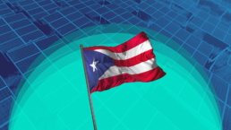 Puerto Rico flag in front of field of solar panels producing renewable energy