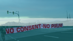Protestors hold a No Consent, No Pipeline banner across the road