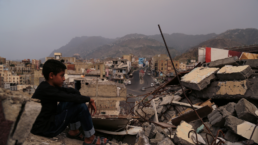 A child from Taiz City sits on the ruins of his ruined home