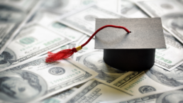 A graduation cap sits atop a pile of money