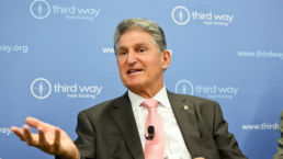 Joe Manchin wears a suit and speaks at an event with a blue background