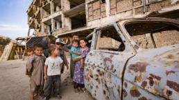 Children play around bullet-riddled car in Kabul