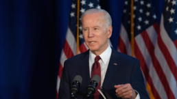 Joe Biden delivers remarks standing behind a podium with American flags in the background