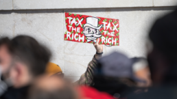 protest sign that says tax the rich featuring monopoly man face
