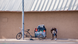 A homeless man hauling recyclables with a flat tire on a hot summer day takes a moment to catch his breath.