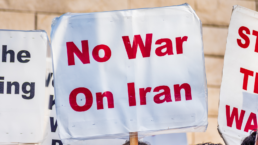 A protestor holds a no war on Iran sign, red text on a white background