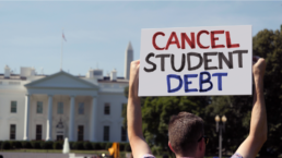 A man holds an CANCEL STUDENT DEBT protest sign in front of the White House on a sunny summer day.