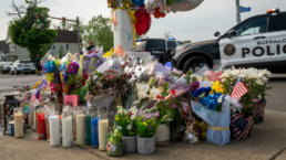 Memorial with flowers and candles to honor the victims of the mass shooting at the Tops market in Buffalo NY. A police SUV is turning the corner in the background