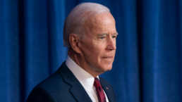 Joe Biden looks into the distance with a blue curtain hanging behind him