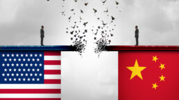 The US and Chinese flags with a person standing on each side of a disintegrating bridge above the flags