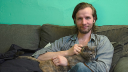 daniel hale sits holding a cat on a couch against a green wall