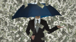 A man with an umbrella obscuring his face stands in a money shower