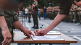 One soldier shows another where to sign on a piece of paper
