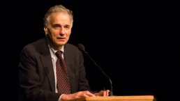Ralph Nader speaks at a podium with a black background