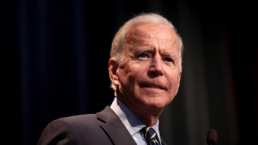 Joe Biden stands against a black background, grimacing
