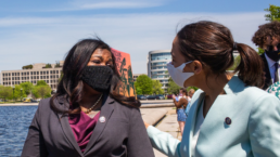 AOC and Cori Bush talk to each other with an urban landscape and a river in the background