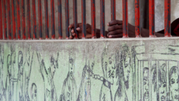 Prisoners put their hands through the bars where a mural depicting slavery is painted