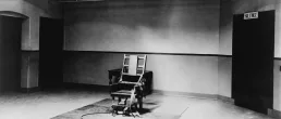 An empty electric chair at the end of the a room, black and white