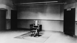 An empty electric chair at the end of the a room, black and white