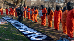 Protestors wear orange jumpsuits and black hoods at a Guantanamo Bay protest