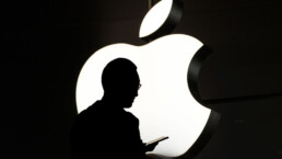 Silhouette of a person using mobile phone in front of the Apple logo