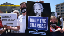 julian assange supporter with sign that says drop the charges