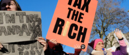 Protesters stand on Whitehall in London to protest for equality in our economy. A placard reads 'Tax the Rich'.