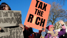 Protesters stand on Whitehall in London to protest for equality in our economy. A placard reads 'Tax the Rich'.