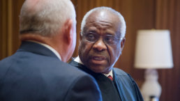 Clarence Thomas talks to someone in his robes