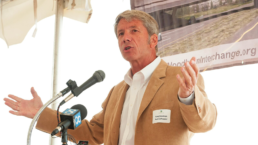 kurt schrader speaks at an event in a nice, tan suit