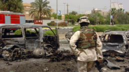 a soldier looks at burned out cars in iraq