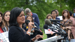 Jayapal stands at a podium holding a microphone