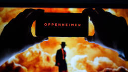 Oppenheimer displayed on phone with explosion and silhouette of Oppenheimer in background