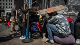 Migrants use cardboard boxes to shield themselves from the sun's heat during the early afternoon on the Roosevelt Hotel migrant waiting line