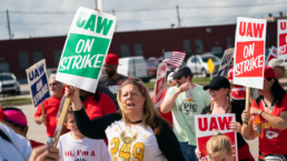 a woman holds a sign at a uaw autoworkers strike