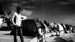 asylum seekers wait by tents in a coastal european city