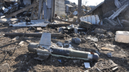 an unexploded missile lies amid ruins