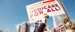 someone holds a sign at a medicare for all rally