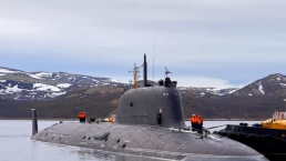 a nuclear submarine docked with workers on its deck