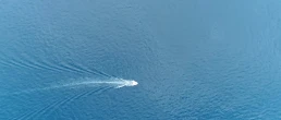 Aerial top down picture of speedboat powerboat moving fast over tropical azure blue colored ocean also showing the white foam left behind by the full powered propellers behind the boat