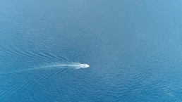 Aerial top down picture of speedboat powerboat moving fast over tropical azure blue colored ocean also showing the white foam left behind by the full powered propellers behind the boat