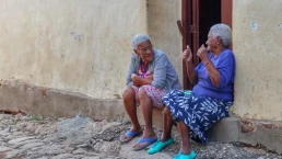 Two old women sitting under the doorway of a home in the colorful town of Trinidad Cuba and talking