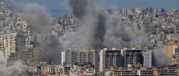 Multiple large plumes of thick grey smoke billow from residential apartment complexes following an explosion or missile strike in a crowded urban skyline. Jan 3 2021 in Iran