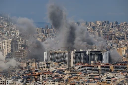 Multiple large plumes of thick grey smoke billow from residential apartment complexes following an explosion or missile strike in a crowded urban skyline. Jan 3 2021 in Iran
