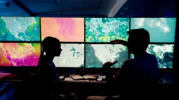 Computer, screen and maps with people in control room for storm tracking, satellite forecast or planning weather pattern. Back, meteorology team or radar data for climate monitor, silhouette or night